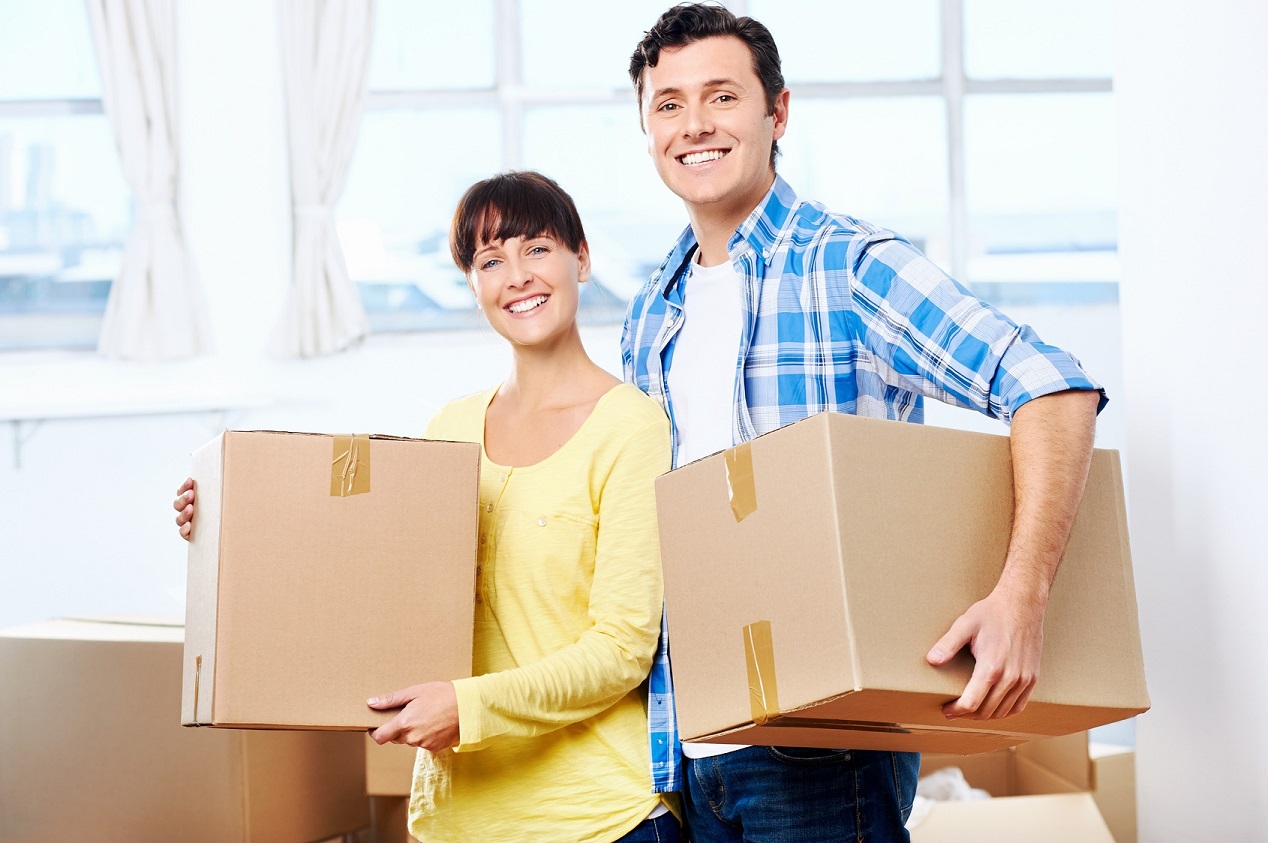 Happy couple carrying boxes moving into new home apartment house